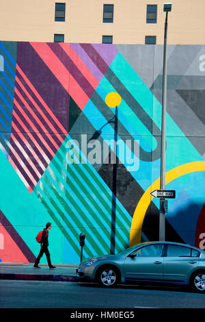 Uomo che cammina nella parte anteriore del grande murale geometrico sul muro nel centro cittadino di Los Angeles in California Foto Stock