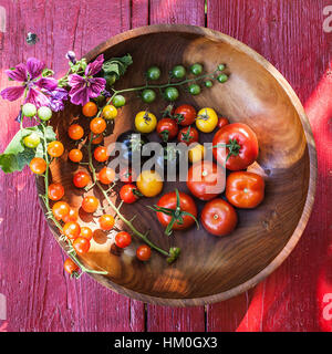 Varietà di cimelio di pomodori in un recipiente rustico e sulla luce di una superficie di legno Foto Stock