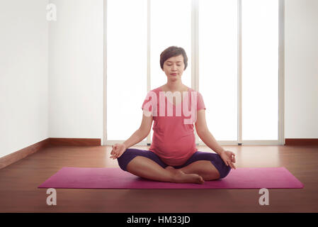 Incinta donna asiatica che esercitano sul tappetino rosa in camera Foto Stock