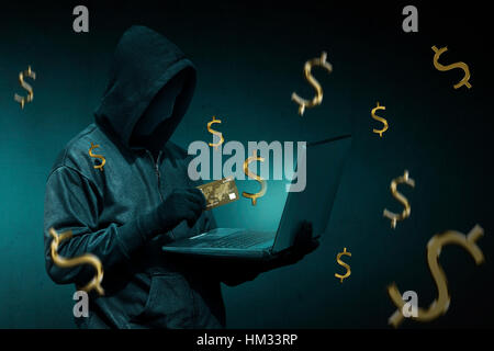 Hacker incappucciato con carta di credito a rubare i dati da un computer portatile su sfondo scuro Foto Stock