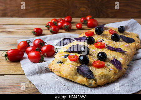 Focaccia alle olive, pomodoro ciliegino e le foglie di basilico. In casa tradizionale pane italiano con erbe sul tovagliolo di lino. Foto Stock