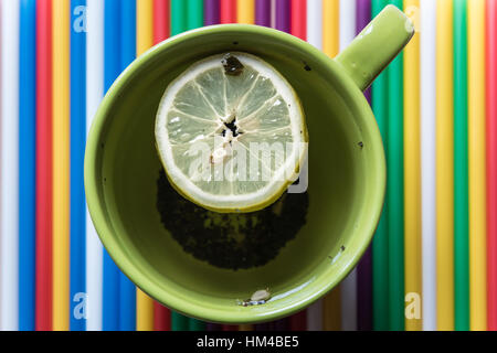 Green tazza di tè con limone su un luminoso colorato sfondo a strisce Foto Stock