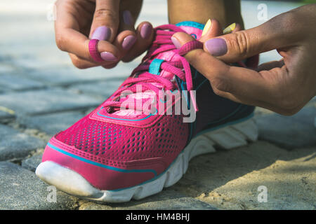 Mani di una giovane donna lacci rosa chiaro e blu sneakers. Scarpe in piedi sul pavimento di pietre e sabbia. In mani femminili viola-giallo manicure Foto Stock