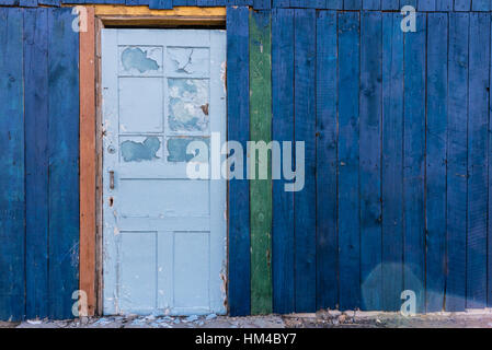 In legno antico azzurro porta in un blu scuro muro. In legno edificio colorato. Condizione di abbandonati. Le schede sono dipinte in colori diversi. Foto Stock