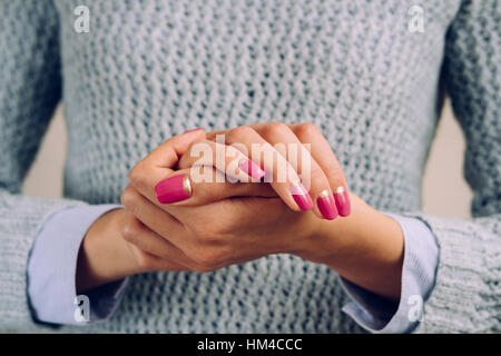 Manicure brillante su mani femminili. La donna in un grigio felpa lavorata a maglia di colore rosa e golden manicure closeup. Foto Stock