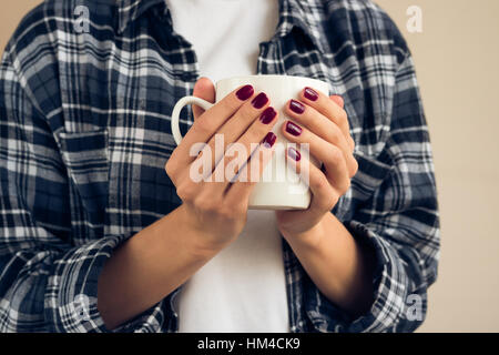 Una donna con il borgogna manicure in plaid shirt holding tazza bianca Foto Stock