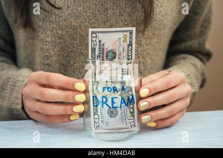 Ragazza di colore marrone maglione giallo con manicure tenendo un vasetto di vetro con il denaro, close-up Foto Stock