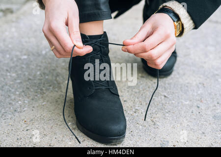 Donna in abiti eleganti lacci delle scarpe di legatura sulle scarpe vicino. Lacci delle scarpe slegato durante una passeggiata in città Foto Stock