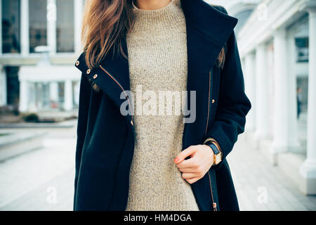 Dettagli di abbigliamento femminile. Close-up di una donna in un maglione, un cappotto e un orologio da polso. Lei ha i capelli marrone e rosso manicure. Foto Stock