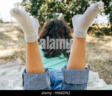 Ragazza in jeans e una maglietta giace su un prato nel parco e la lettura di un libro. Vista dal retro. Foto Stock