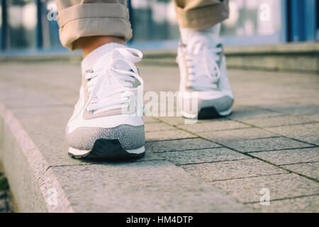 I piedi femminili in bianco sneakers camminando sul marciapiede, basso angolo, colori retrò. Foto Stock