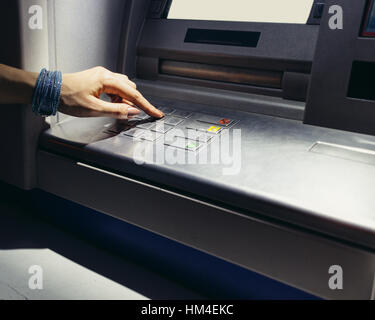 Mano femmina inserendo il codice segreto nell'ATM di notte sulla strada Foto Stock