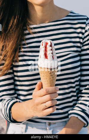 Close-up di gelato in una mano femminile, una donna con capelli castani e una camicia a righe tenendo un gelato all'aperto in estate Foto Stock