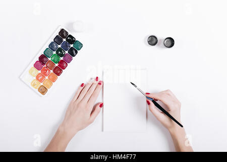 Le mani delle donne con il rosso smalto per unghie verniciate acquerelli in un notebook, vista dall'alto Foto Stock