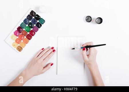 Mani femminili con manicure rosso dipinto acquerelli in un notebook, vista dall'alto Foto Stock