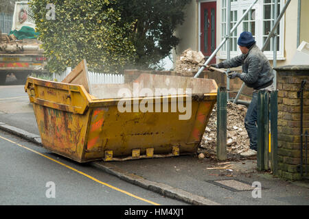 Costruttori rifiuti cassonetto, sul marciapiede & giallo, linea essendo riempito / caricato builder caricamento mentre salta il camion attende. Regno Unito Foto Stock