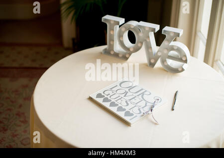Wedding guestbook seduto su una tabella con una grande parola amore a un matrimonio in Sussex, Regno Unito. Gli ospiti firmare con i loro messaggi di cuore Foto Stock