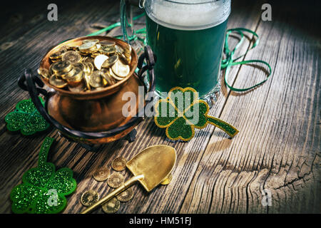 Pentola d'oro con pala, birra e trifogli su sfondo di legno Foto Stock