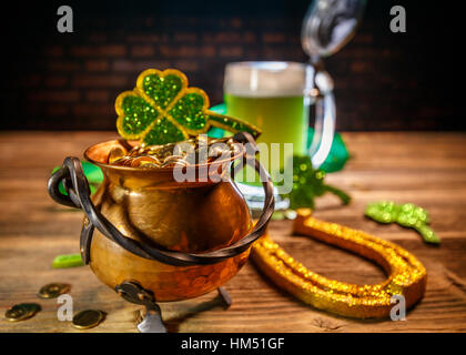 Pentola d'oro con pala, birra e trifogli su sfondo di legno Foto Stock