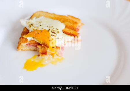 Avanzi di prosciutto e formaggio toast con uovo fritto sopra con morsi mancanti. Foto Stock