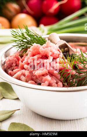 Materie di carne macinata in vaschetta bianca. Di carne macinata di maiale su uno sfondo di fresche verdure organiche Foto Stock