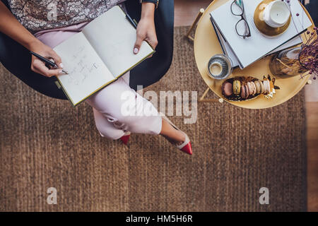 Immagine ritagliata di imprenditrice iscritto nel diario mentre è seduto su una sedia da tavolo a home office Foto Stock