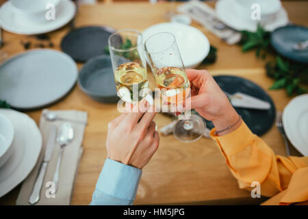 Immagine ritagliata di amici di tostatura flauti di champagne mentre è seduto al tavolo da pranzo Foto Stock