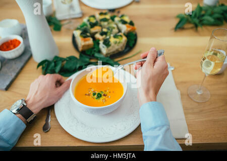 Immagine ritagliata dell'uomo avente la zuppa di zucca al tavolo da pranzo Foto Stock