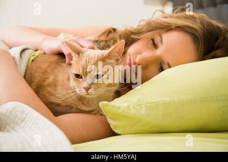 Ragazza adolescente (16-17) giacente in letto con carezze e il ginger tabby cat Foto Stock