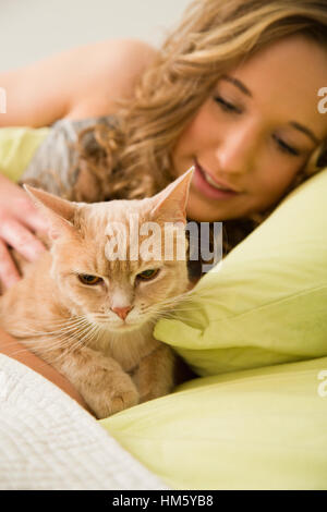 Ragazza adolescente (16-17) che giace nel letto e accarezzare lo zenzero tabby cat Foto Stock