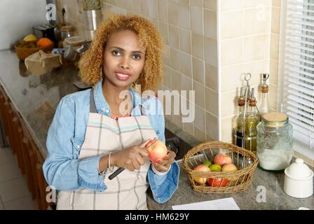 Giovane africano donna americana sbucciare le mele, in cucina Foto Stock