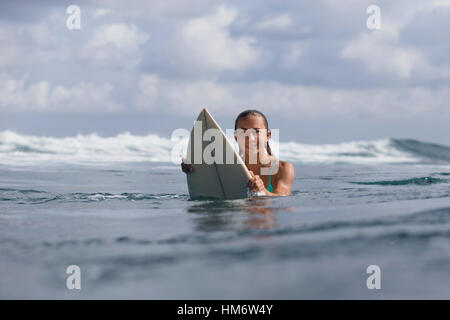 Ritratto di donna tenendo la tavola da surf in mare contro sky Foto Stock