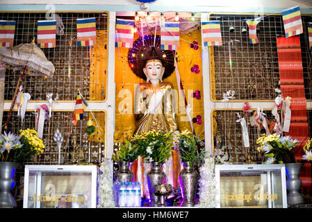 Interno del Santuario del Buddha Dorato di Mingun Pahtodawgyi Myanmar | MINGUN, Myanmar — Un Buddha dorato in piedi, avvolto in un drappo dorato e incorniciato da bandiere buddiste Theravada, domina una sala del santuario costruita alla base del Mingun Pahtodawgyi. L'immagine occupa la parte inferiore in mattoni massicci dello stūpa incompiuto che il re Bodawpaya iniziò nel 1790, intendendolo come il più grande stūpa del mondo prima che la costruzione fosse abbandonata decenni dopo. Foto Stock