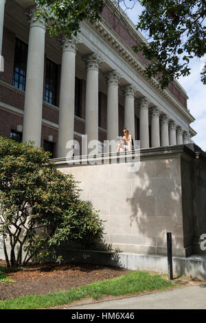 Una studentessa si siede al sole a studiare con enormi colonne di uno degli edifici accademici presso la Harvard University che incombe in background. Foto Stock