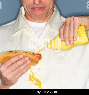 Uomo maturo holding hotdog e fuoriuscita accidentalmente la senape sulla camicia Foto Stock