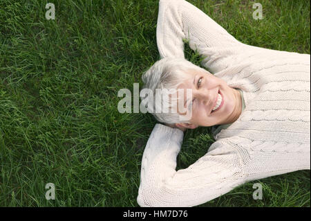 Sorridente donna matura sdraiati sull'erba Foto Stock