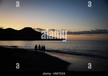 Silhouette di quattro persone che passeggiano lungo la spiaggia al tramonto Foto Stock