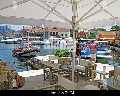 Ristorante sul mare da sotto ombrellone di barche da pesca e yacht ormeggiati nel porto di Fiskardo sull'isola greca di Cefalonia Foto Stock