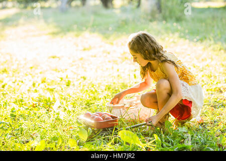 Ragazza con frutta accovacciato in erba Foto Stock