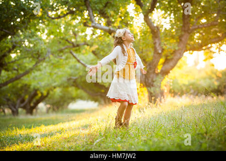 Spensierata ragazza di filatura in frutteto con le braccia tese Foto Stock