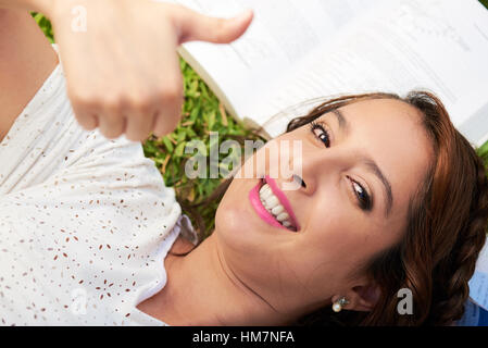 Ragazza facendo pollice in su mentre che stabilisce su libri Foto Stock