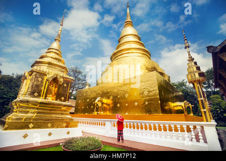 Donna con turistico rosso tailandese tradizionale ombrellone vicino a Golden Stupa al tempio di Wat Phra Singh in Chiang Mai Thailandia Foto Stock