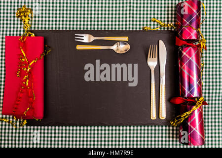 Luogo previsto per la cena di Natale, coltello, forchetta, Christmas Cracker, igienico sul tappeto di ardesia. Foto Stock