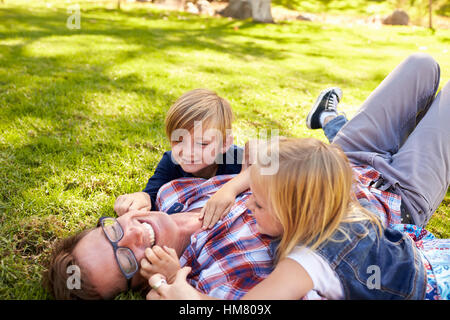 Due ragazzi che giocano con i loro papà, giacente in un parco, vista laterale Foto Stock