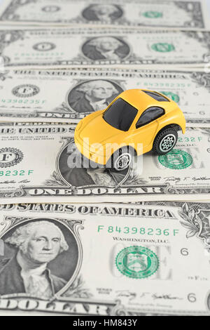 Piccolo giallo giocattolo auto a noi 1 Dollaro / 1 $ fatture. Come metafora per il costo dell'automobilismo e della benzina in noi. Foto Stock