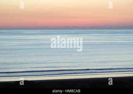 Il sole è appena sceso dalla vista sull'Oceano Pacifico e il cielo è illuminato con rosa, viola e sfumature di arancione come le onde si infrangono sulla riva. Foto Stock