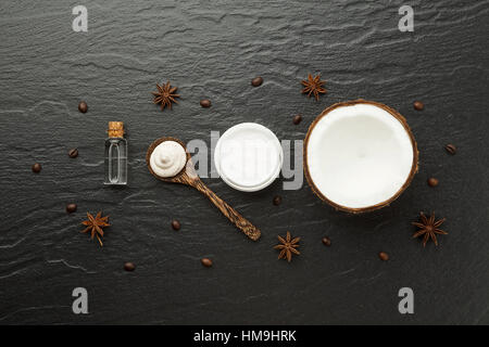 In casa i prodotti spa. Metà di guscio di noce di cocco, caffè e anice su sfondo nero. Olio, lozione e la macchia sul cucchiaio di legno dalla vista dall'alto. Buona per lo spazio di un Foto Stock