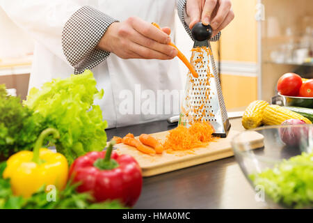 Lo chef triturazione di carote con grattugia in cucina Foto Stock