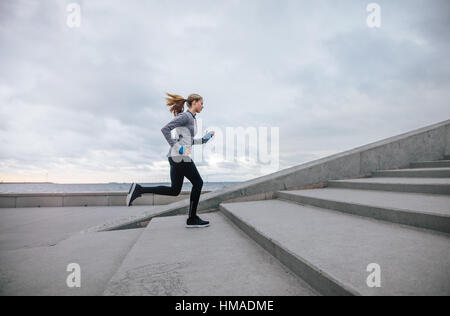 Vista laterale colpo di donna fitness in esecuzione su fasi. Femmina atleta runner salendo le scale. Foto Stock