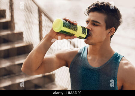 Immagine ravvicinata di montare il giovane uomo acqua potabile dalla spiaggia dopo l'allenamento. Runner acqua potabile dopo esercizio. Foto Stock